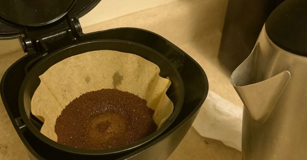 Drip coffee maker with pre-wet grounds in a paper filter and kettle nearby on a kitchen counter